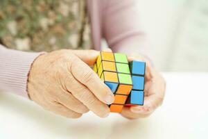 Bangkok, thailand - Maj 15, 2022 asiatisk äldre kvinna spelar rubik kub spel till öva hjärna Träning för hjälp demens förebyggande och alzheimers sjukdom. foto