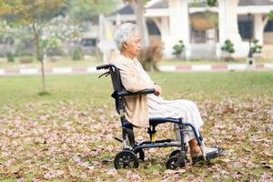 asiatisk senior eller äldre gammal damkvinna tålmodig sitt knä på rullstol i park, hälsosamt starkt medicinskt koncept.