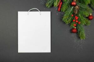 jul festlig platt lägga sammansättning med vit gåva handla väska mockup, röd bollar dekoration, bär och gran träd grenar på röd bakgrund. topp se. kopia Plats. foto