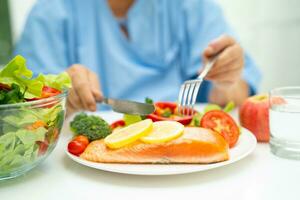 asiatisk äldre kvinna patient äter lax biff frukost med vegetabiliska friska mat i sjukhus. foto