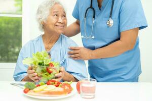 asiatisk äldre kvinna patient äter lax biff frukost med vegetabiliska friska mat i sjukhus. foto