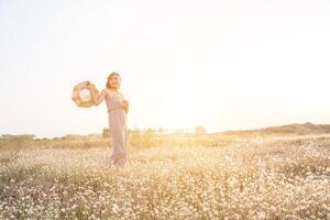 sexig vacker kvinna som står i blommafält och håller sin hatt foto