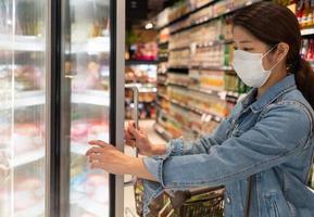 ung asiatisk kvinna som bär mask medan hon handlar mat i stormarknaden foto