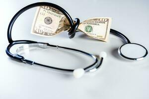 hög kosta av medicinsk hälsa med stetoskop. stetoskop insvept runt om pengar isolerat, stetoskop bunden med dollar räkningar foto