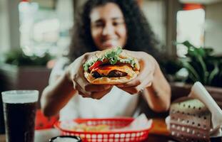 leende flicka som visar en burger i en restaurang. närbild av en kvinna som visar aptitlig hamburgare i en restaurang foto