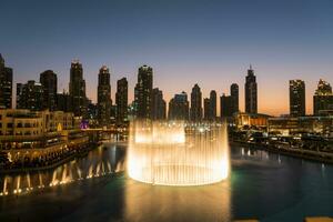 dubai sång fontäner på natt sjö se mellan skyskrapor. stad horisont i skymning modern arkitektur i uae huvudstad stadens centrum. foto