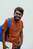 indisk studerande med blå ryggsäck, glasögon och anteckningsbok Framställ på grå bakgrund. de begrepp av utbildning och skolutbildning. tid till gå tillbaka till skola foto