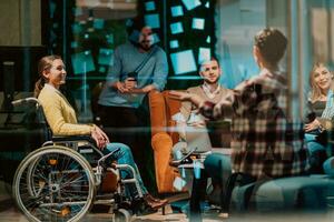 affärskvinna i rullstol har företag möte med team på modern kontor. en grupp av ung frilansare hålla med på ny uppkopplad företag projekt foto