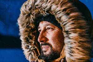 huvud skott av en man i en kall snöig område bär en tjock brun vinter- jacka, snö glasögon och handskar på en kall scandinavian natt. liv i de kall regioner av de Land. foto