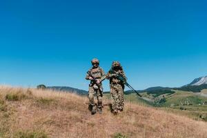 en prickskytt team trupp av soldater är gående hemlig. prickskytt assistent och team ledare gående och siktar i natur med gul gräs och blå himmel. taktisk kamouflage enhetlig. foto