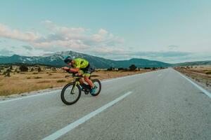 full längd porträtt av ett aktiva triathlete i sportkläder och med en skyddande hjälm ridning en cykel. selektiv fokus foto