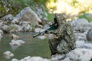en militär man eller airsoft spelare i en kamouflage kostym smygande de flod och syftar till från en prickskytt gevär till de sida eller till mål. foto