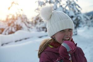 söt liten flicka medan äter istapp på skön vinter- dag foto