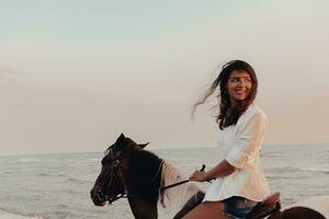 kvinna i sommar kläder åtnjuter ridning en häst på en skön sandig strand på solnedgång. selektiv fokus foto