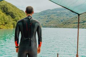 idrottare sätta på en simning kostym och framställning för triathlon simning och Träning i de flod omgiven förbi naturlig grönska foto