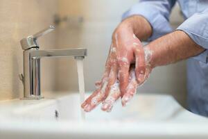 man använder sig av tvål och tvättning händer under de vatten knacka. hygien begrepp hand närbild detalj. foto