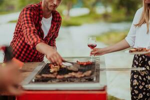 Lycklig par toasting röd vin glas medan har picknick franska middag fest utomhus- under sommar Semester semester nära de flod på skön natur foto