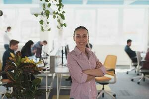 porträtt av ung leende företag kvinna i kreativ öppen Plats coworking börja kontor. framgångsrik affärskvinna stående i kontor med copyspace. medarbetare arbetssätt i bakgrund. foto