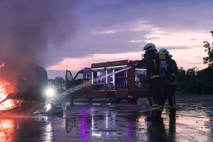 brandmän använder sig av vatten brand eldsläckare till stridande med de brand flamma i bil olycka. brandman industriell och offentlig säkerhet begrepp rädda i natt. foto