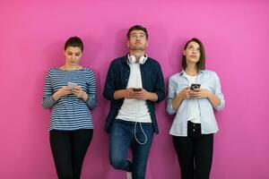 olika tonåringar använder sig av smartphone medan Framställ för en studio Foto i främre av en rosa bakgrund