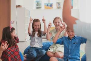 en Lycklig kvinna lärare Sammanträde och spelar hand spel med en grupp av liten skolbarn foto