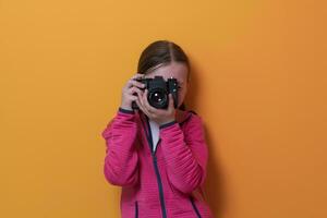 liten flicka fotograf isolerat på gul bakgrund leende tar foton med en retro årgång kamera.