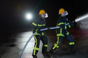 brandmän använda sig av en vatten slang till eliminera en brand fara. team av brandmän i de farlig rädda uppdrag. foto