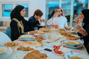 muslim familj har iftar middag dricka vatten till ha sönder fest. äter traditionell mat under ramadan festande månad på Hem. de islamic halal äter och dricka i modern Hem foto