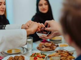 modern multietnisk muslim familj delning en skål av datum medan njuter iftar middag tillsammans under en ramadan fest på Hem foto