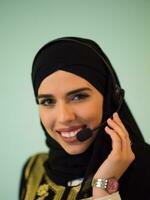 porträtt av muslim kvinna med hijab scarf kund representativ företag kvinna med telefon headsetet portion och stödjande uppkopplad med kund i modern ring upp Centrum isolerat på cyan bakgrund foto