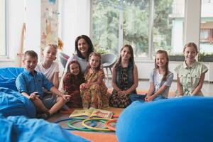 en Lycklig kvinna lärare Sammanträde och spelar hand spel med en grupp av liten skolbarn foto