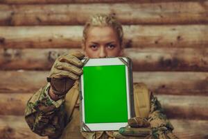kvinna soldat använder sig av läsplatta dator mot gammal trä- vägg i läger foto