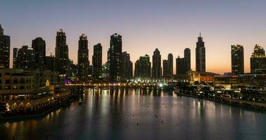 dubai sång fontäner på natt se mellan skyskrapor. Timelapse av stad horisont i skymning modern arkitektur och lång företag och bosatt byggnader i uae huvudstad. foto