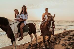 de familj spenderar tid med deras barn medan ridning hästar tillsammans på en sandig strand. selektiv fokus foto