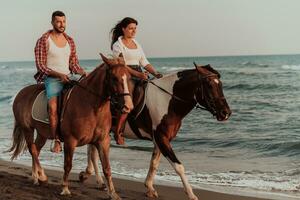 en kärleksfull par i sommar kläder ridning en häst på en sandig strand på solnedgång. hav och solnedgång i de bakgrund. selektiv fokus foto