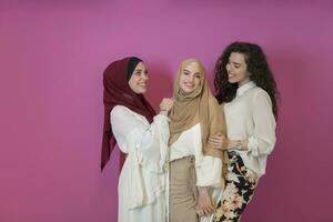 grupp av skön muslim kvinnor två av dem i modern klänning med hijab använder sig av mobil telefon isolerat på rosa bakgrund representerar modern islam mode teknologi och ramadan kareem begrepp foto