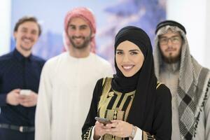 grupp porträtt av ung muslim människor kvinnor i modern hijab klänning med tre arab män använder sig av smartphones på modern ljus Hem foto