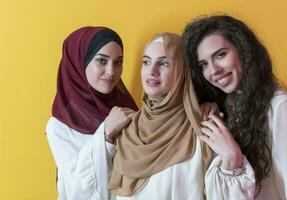 grupp porträtt av skön muslim kvinnor två av dem i en modern klänning med hijab isolerat på en gul bakgrund foto