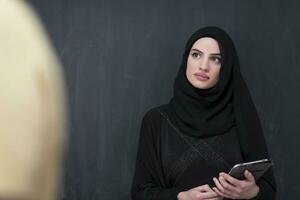 ung modern muslim företag kvinna använder sig av smartphone bär hijab kläder i främre av svart svarta tavlan foto