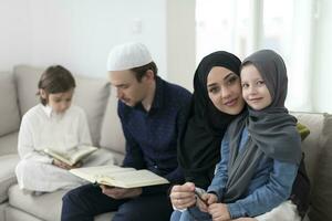 traditionell muslim familj föräldrar med barn läsning quran och bön- tillsammans på de soffa innan iftar middag under en ramadan fest på Hem foto