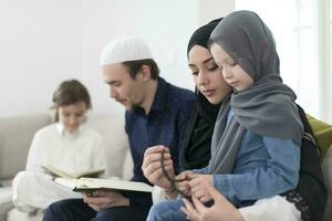 traditionell muslim familj föräldrar med barn läsning quran och bön- tillsammans på de soffa innan iftar middag under en ramadan fest på Hem foto