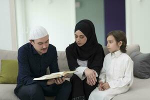 traditionell muslim familj föräldrar med barn läsning quran och bön- tillsammans på de soffa innan iftar middag under en ramadan fest på Hem foto