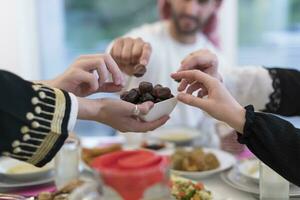 modern multietnisk muslim familj delning en skål av datum medan njuter iftar middag tillsammans under en ramadan fest på Hem foto