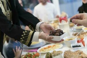 modern multietnisk muslim familj delning en skål av datum medan njuter iftar middag tillsammans under en ramadan fest på Hem foto