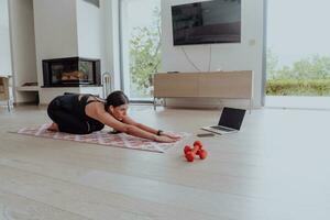 ung skön kvinna tränar, stretching och praktiserande yoga med tränare via video ring upp konferens i ljus solig hus. friska livsstil, välbefinnande och mindfulness begrepp. foto
