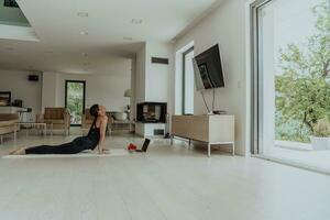 ung skön kvinna tränar, stretching och praktiserande yoga med tränare via video ring upp konferens i ljus solig hus. friska livsstil, välbefinnande och mindfulness begrepp. foto