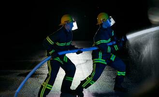 brandmän använda sig av en vatten slang till eliminera en brand fara. team av brandmän i de farlig rädda uppdrag. foto