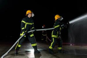 brandmän använder sig av en vatten slang till eliminera en brand fara. team av kvinna och manlig brandmän i farlig rädda uppdrag. foto