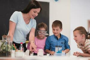 elementärt skola vetenskap klassrum entusiastisk lärare förklarar kemi till olika grupp av barn, liten pojke blandar kemikalier i bägare. barn lära sig med intressera foto