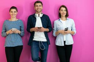 olika tonåringar använder sig av smartphone medan Framställ för en studio Foto i främre av en rosa bakgrund